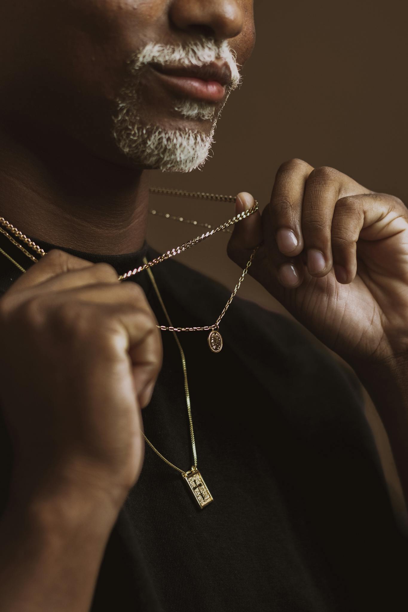 An artistic close-up of a man showcasing intricate gold necklaces in a studio setting.