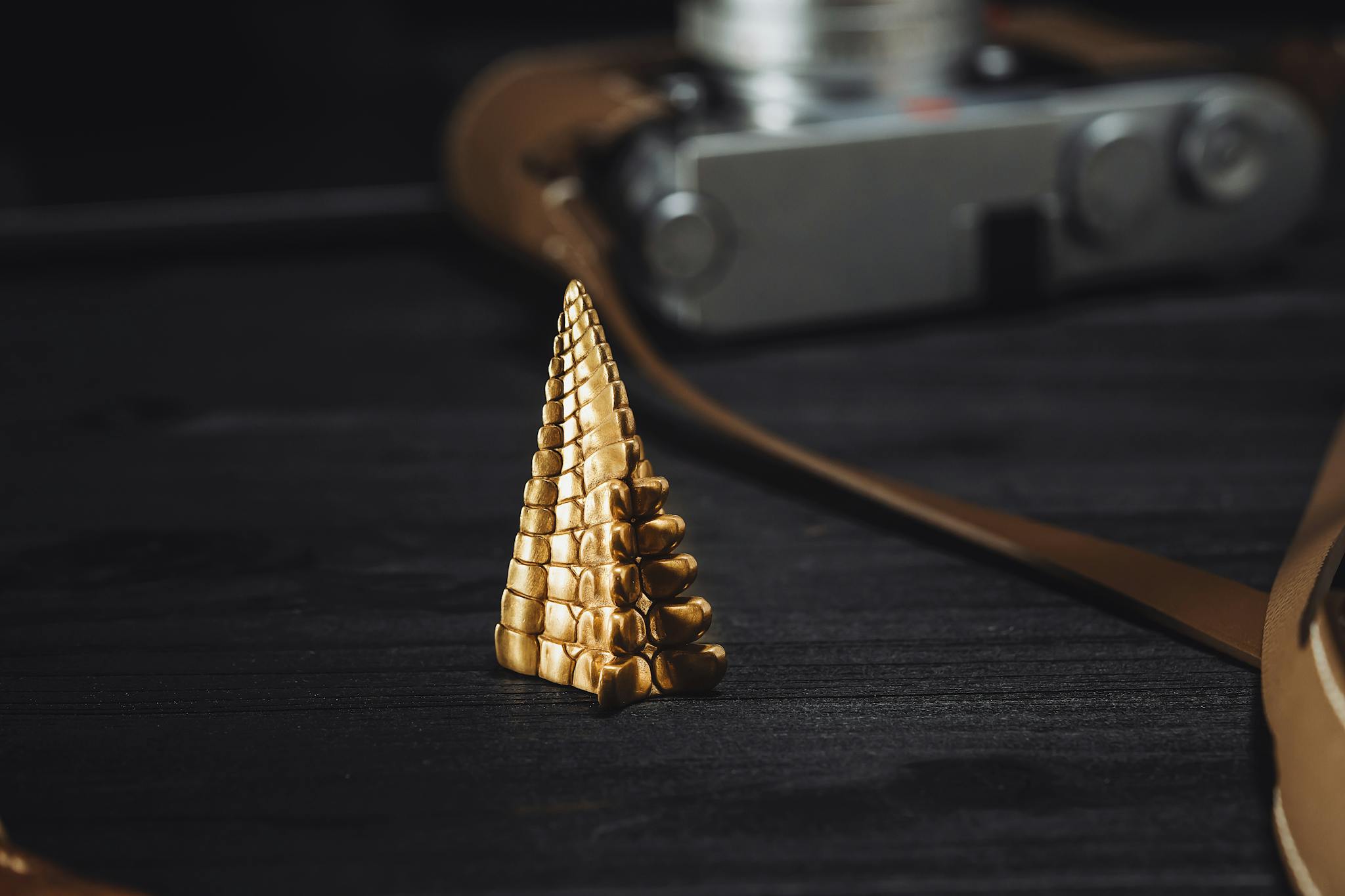 Close-up of a handcrafted golden jewelry piece with leather strap on dark surface. Artistic still life.