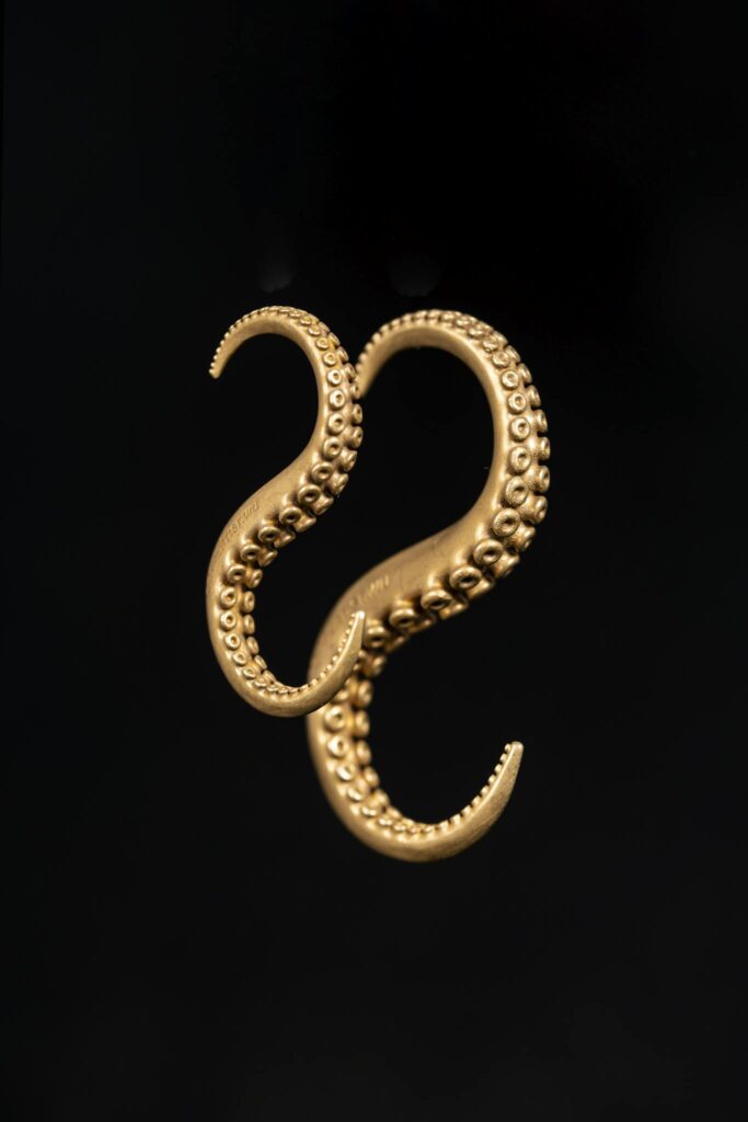 Close-up of copper octopus tentacle earrings on a dark background, showcasing intricate metalwork.