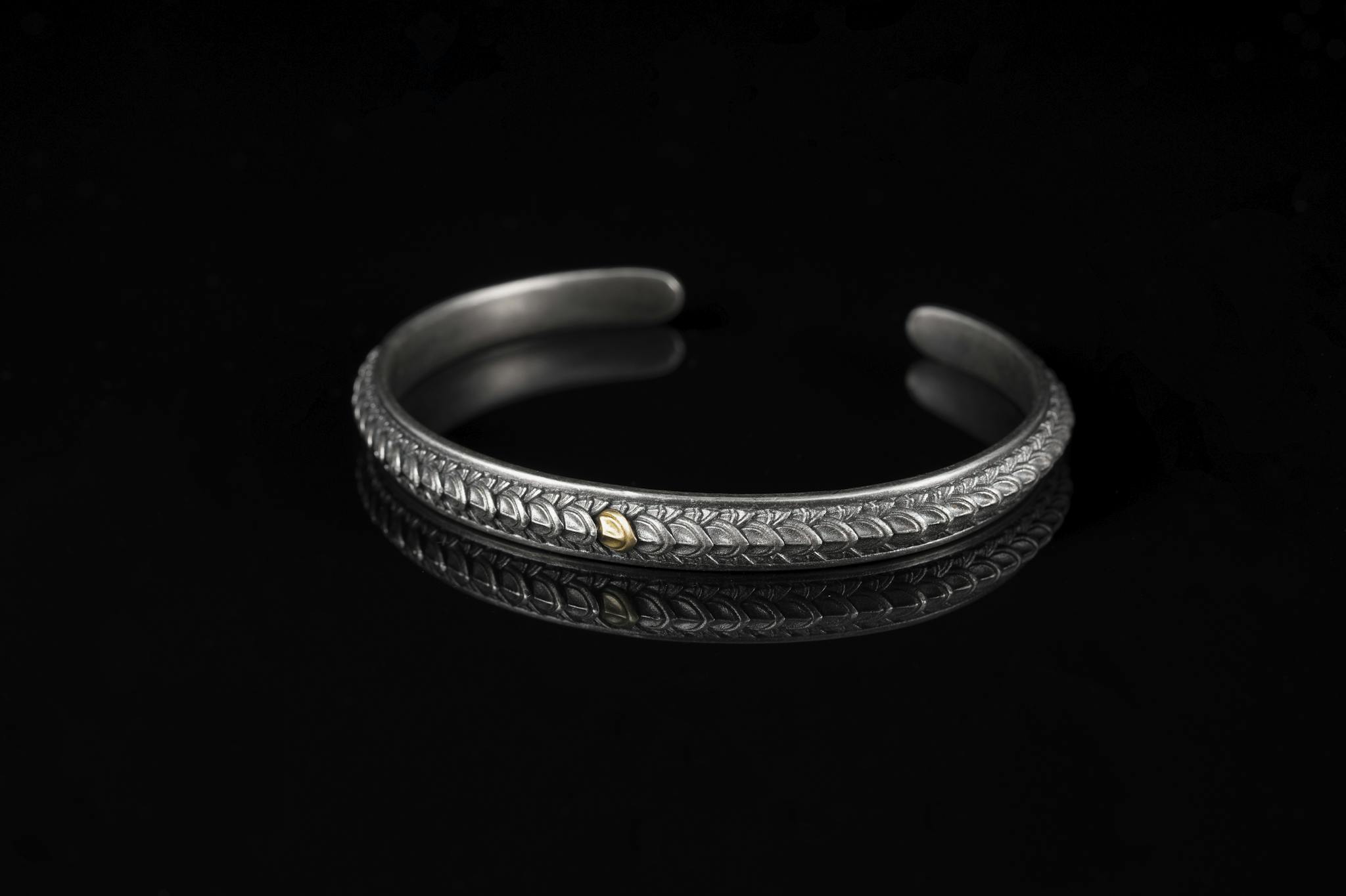 Stylish handmade silver bracelet with intricate detailing, set against a black reflective backdrop.